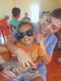 Student holding a child wearing her sunglasses