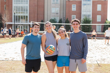 Four students holding a volleyball on the volleyball court