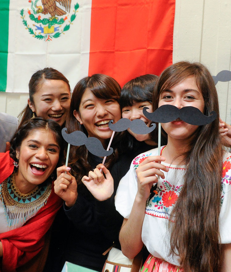 International Students holding paper mustaches in front of a Mexican flag