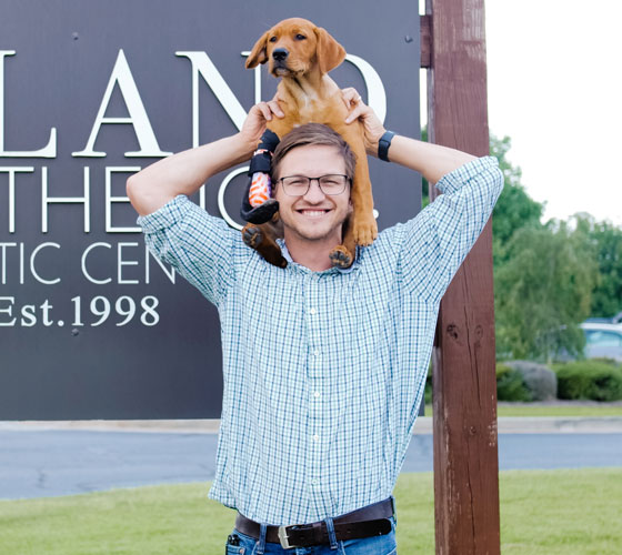 Mercer alumnus, Chris, holding a puppy, Goose, with a prosthetic paw on his shoulders