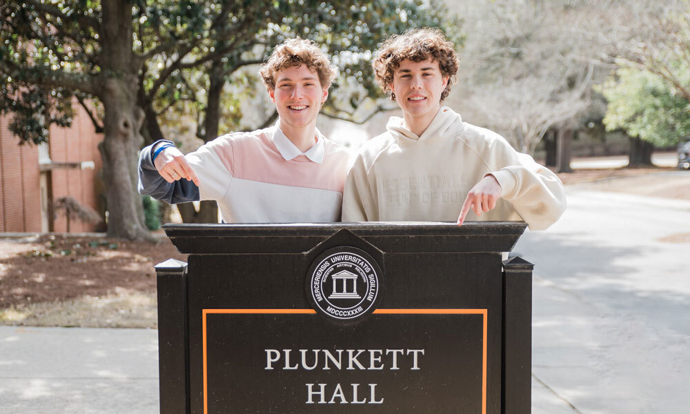 Dylan Sanfilippo and Colin Ralph standing in front of the Plunkett Hall sign