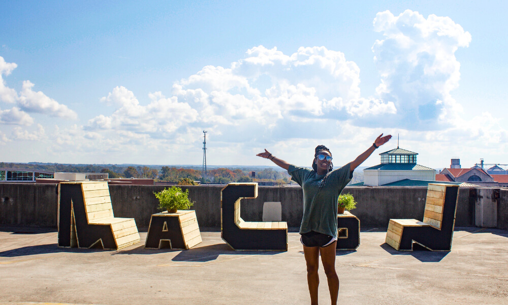 Mercer student posing for a photo in front of an art installation that reads 