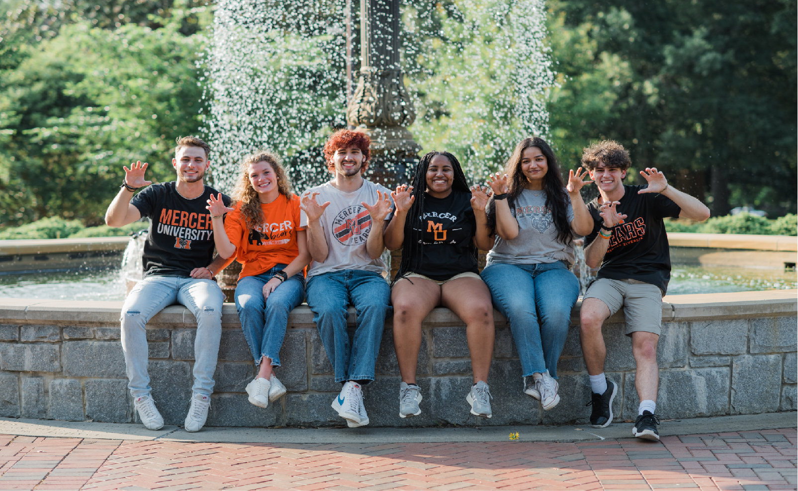 Six students giving the bear in front of a fountain.