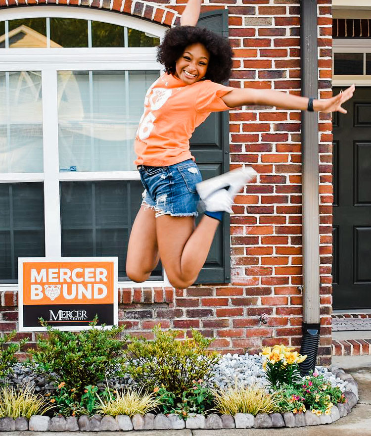 Student jumping in front of a Mercer Bound sign