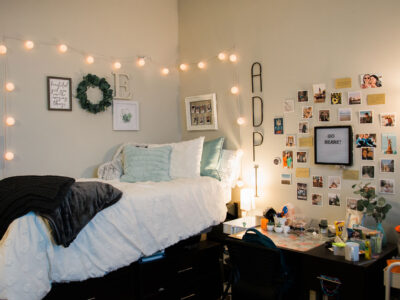A bedroom in Legacy Hall with a bed and desk, and string lights and photos on the wall as decoration.