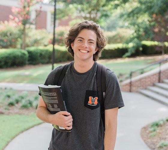 A male student smiling, holding a book