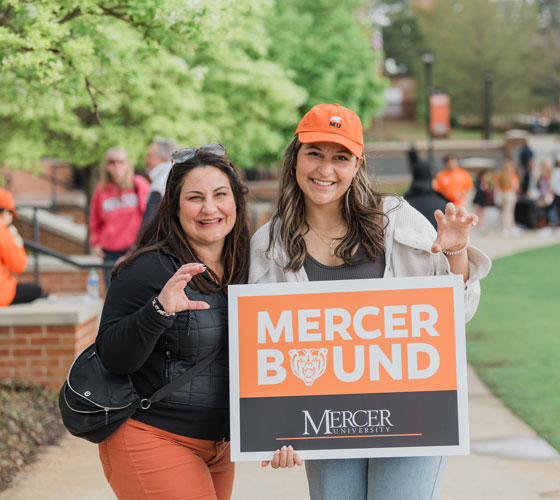 A mother and daughter smiling while holding a MercerBound sign